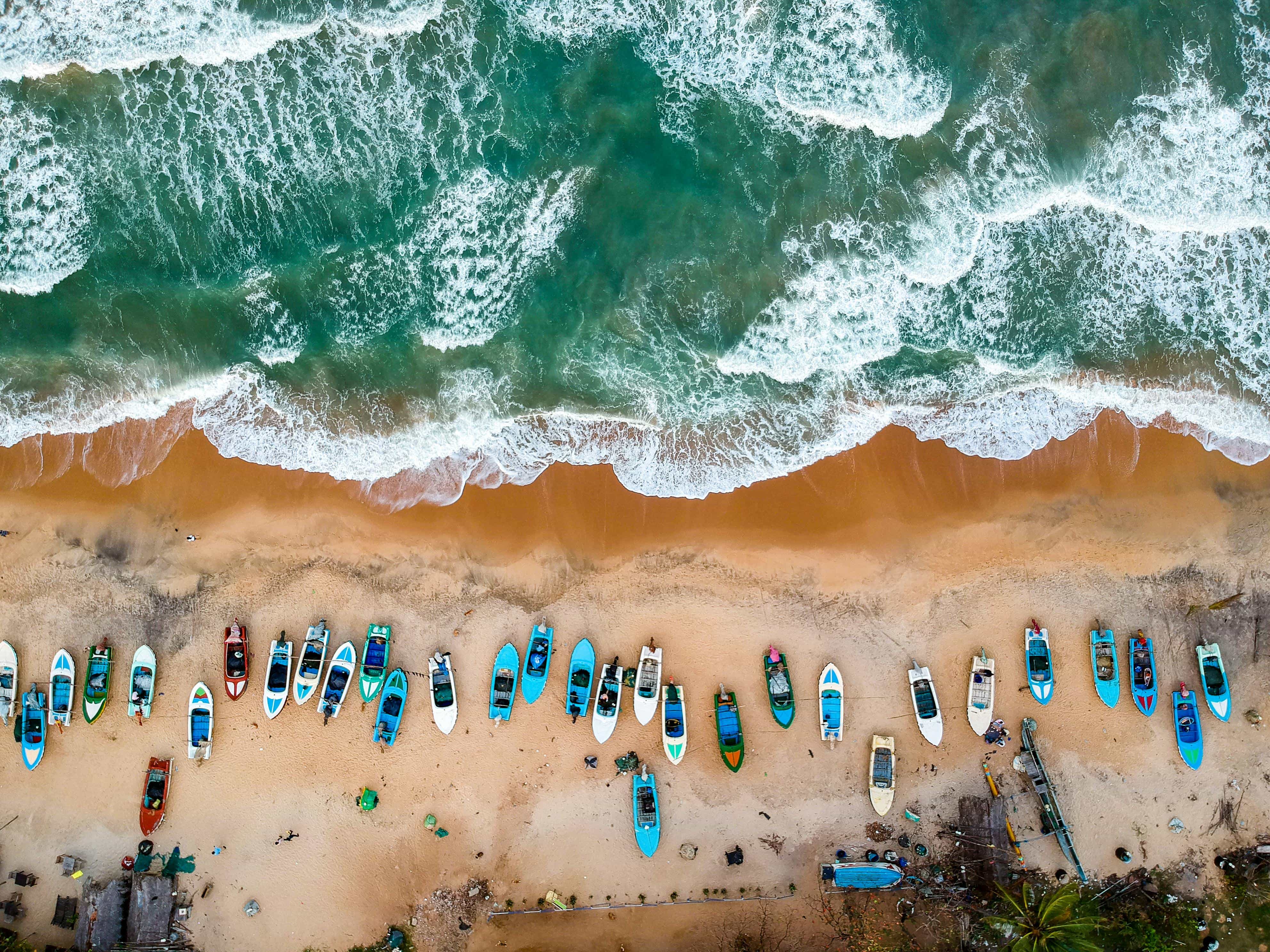 Aerial view of Arugam Bay, Sri Lanka showing turquoise ocean, golden sandy beach, and colorful fishing boats – AASH Travels